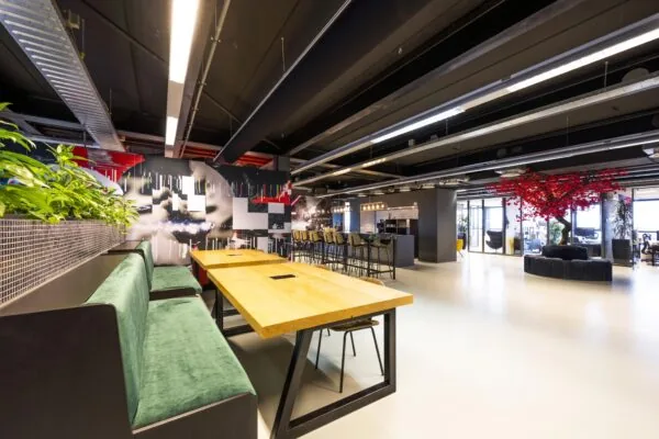 Moderne kantoorruimte aan de Anthony Fokkerweg met werkplekken, een lange houten tafel, groene zitbanken en een opvallende rode boom als eyecatcher.